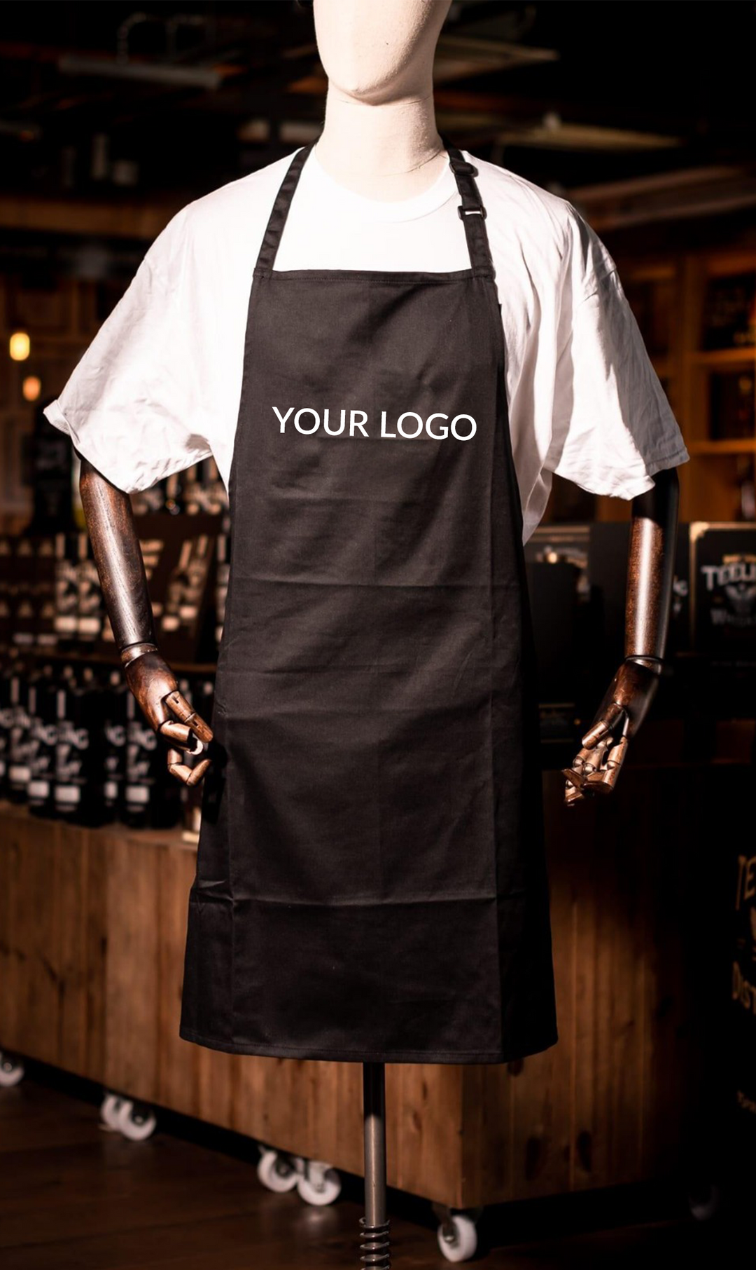 Black custom logo apron worn by hospitality staff, featuring a front pocket and adjustable neck strap for café and restaurant uniforms.